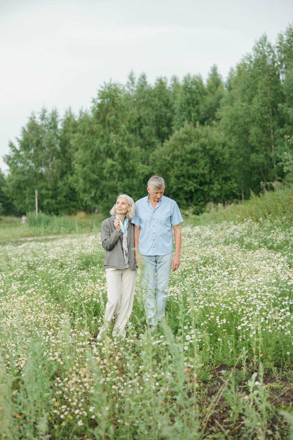 A gray-haired couple walking together through a meadow of wildflowers